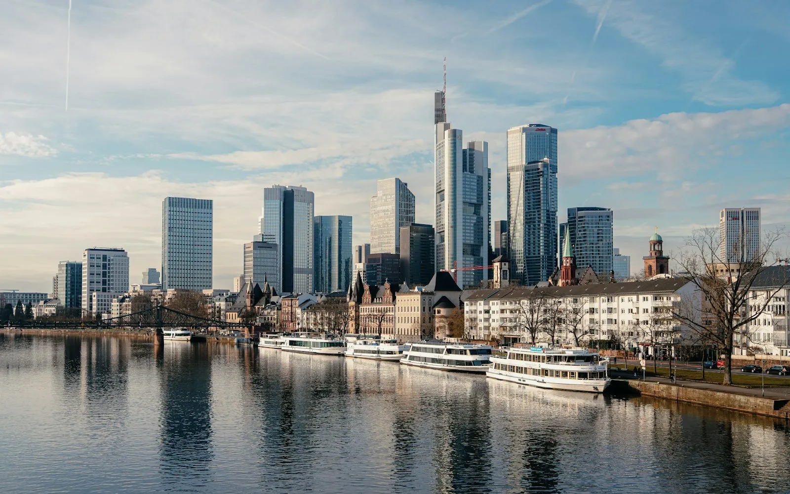 Modern skyscrapers line a river with boats at anchor